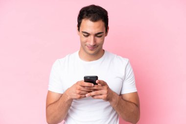 Pembe arka planda cep telefonu kullanan genç beyaz bir adam izole edilmiş.