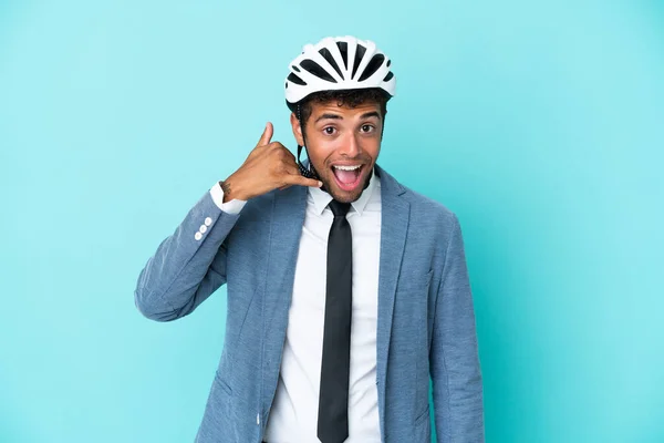 Young business Brazilian man with bike helmet isolated on blue background making phone gesture. Call me back sign