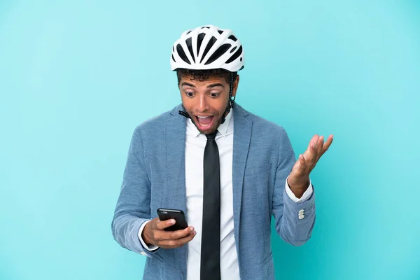 Young business Brazilian man with bike helmet isolated on blue background surprised and sending a message