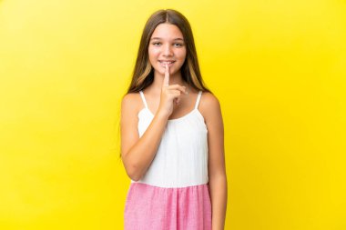 Sarı arka planda izole edilmiş küçük beyaz kız parmağını ağzına koyan sessiz bir jest işareti gösteriyor.