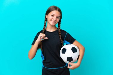 Küçük beyaz kız mavi arka planda izole edilmiş futbol topuyla ve kendisiyle gurur duyuyor.