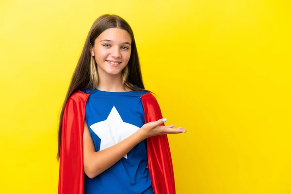小さなCaucasianスーパーヒーロー女の子孤立しました上の黄色の背景を提示しますAアイデアを見ながら笑顔 — ストック写真