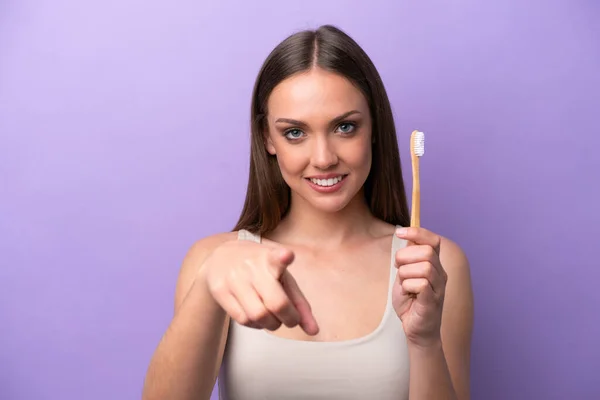 Young caucasian woman brushing teeth isolated on purple background points finger at you with a confident expression