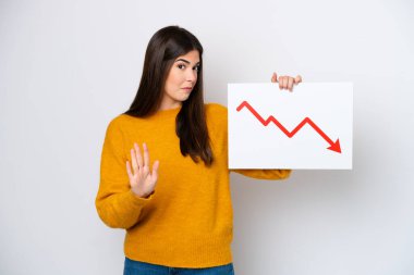 Beyaz arka planda izole edilmiş genç Brezilyalı kadın elinde azalan bir istatistik ok sembolü olan bir tabela tutuyor ve dur işareti yapıyor.
