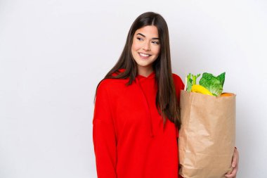 Beyaz arka planda izole edilmiş alışveriş torbası tutan Brezilyalı genç bir kadın yan tarafa bakıyor ve gülümsüyor.