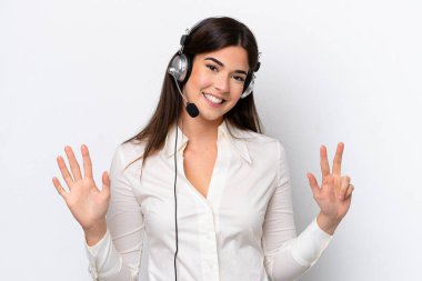 Beyaz arka planda izole edilmiş kulaklıkla çalışan beyaz pazarlamacı kadın parmaklarıyla sekizi sayıyor.