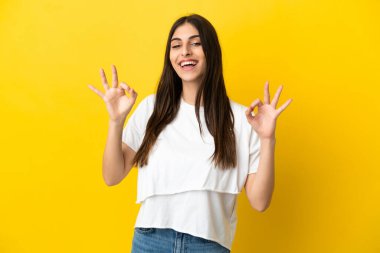 Sarı arka planda izole edilmiş beyaz bir kadın iki eliyle tamam işareti gösteriyor.
