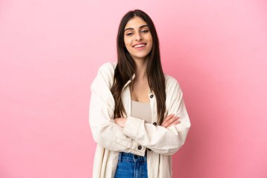 Pembe arka planda izole edilmiş genç beyaz kadın kollarını ön cephede çapraz tutuyor.