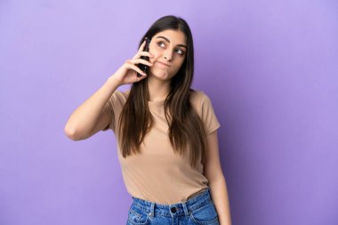 Mor arka planda izole edilmiş cep telefonu kullanan beyaz bir kadın.