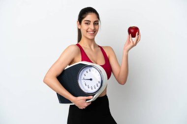 Beyaz arka planda, tartı makinesi ve elmasıyla izole edilmiş genç beyaz bir kadın.