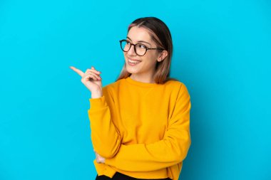 Kafkasyalı genç kadın mavi arka planda izole edildi. Çözümün farkına varmak için parmağını kaldırdı.