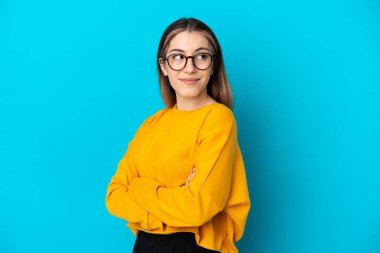 Mavi arka planda izole edilmiş genç beyaz kadın, omuzlarını kaldırırken şüpheyle hareket ediyor.