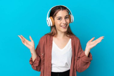 Mavi arka planda izole edilmiş genç beyaz kadın şaşırdı ve müzik dinliyor.