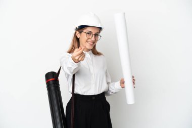 Miğferli ve elinde planları olan genç bir mimar para hareketi yaparak beyaz arka planda izole edilmiş.