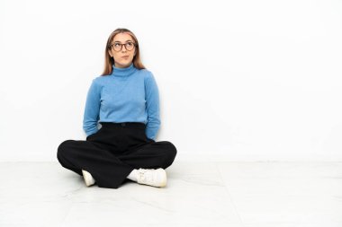 Beyaz bir kadın yerde oturuyor ve kafasını kaldırıyor.