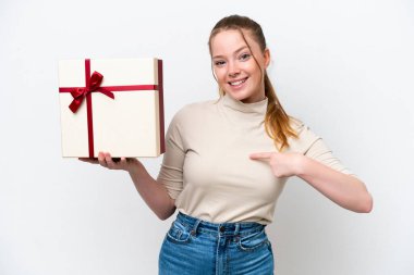 Beyaz arka planda yüzü sürpriz bir ifadeyle izole edilmiş bir hediye tutan beyaz bir kadın.