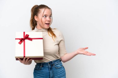 Beyaz arka planda yüzü sürpriz bir ifadeyle izole edilmiş bir hediye tutan beyaz bir kadın.