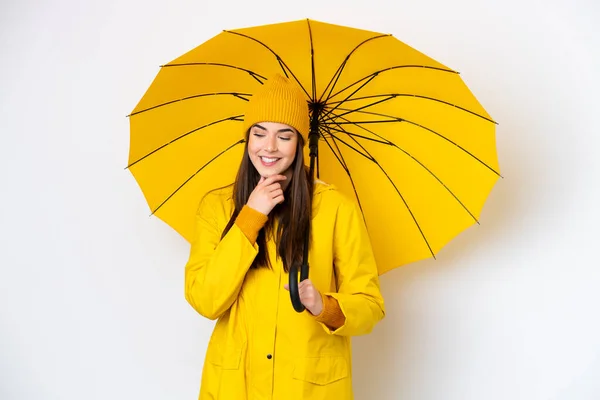 若いですブラジル人女性でレインプルーフコートと傘は白い背景に隔離されました側と笑顔を見て — ストック写真