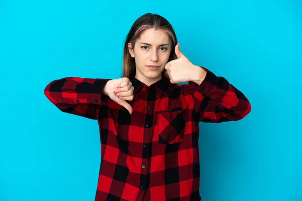 Young caucasian woman isolated on blue background making good-bad sign. Undecided between yes or not