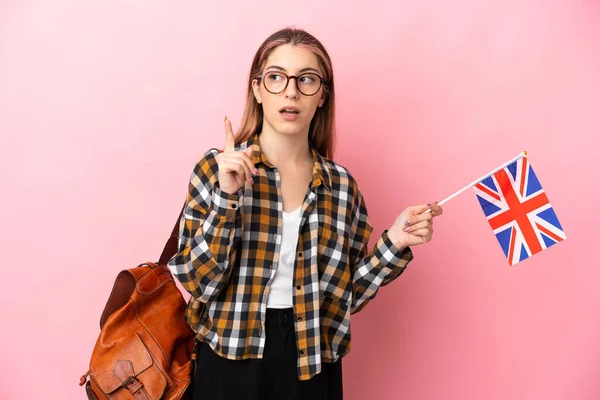 一个年轻的惊慌失措的女人举着一面英国国旗 背景是粉色的 想用手指指指一下 — 图库照片