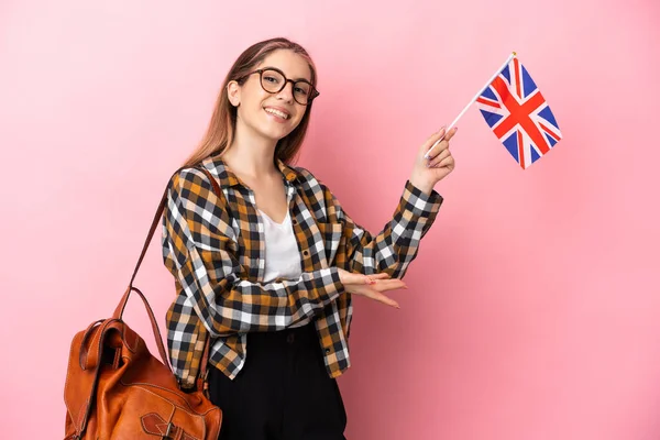 年轻的惊慌失措的女人举着一面英国国旗 与粉红背景隔离 向旁边伸出手来 感谢对方邀请她来 — 图库照片