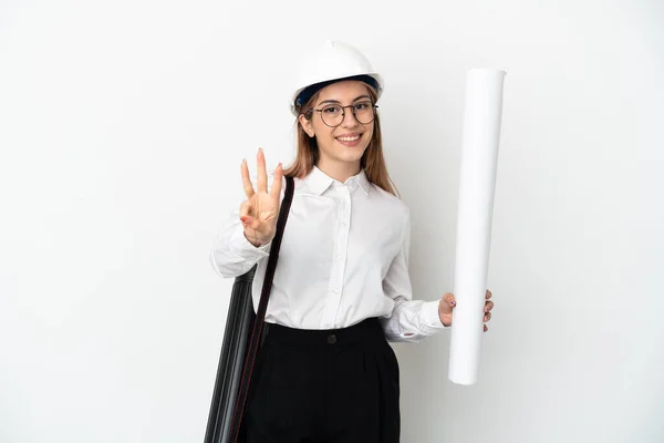 Young architect woman with helmet and holding blueprints isolated on white background happy and counting three with fingers