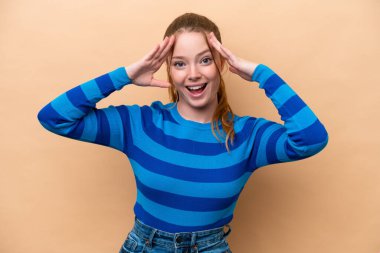 Beyazlı genç bir kadın, bej arka planda izole edilmiş, sürpriz bir ifadeyle.