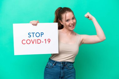 Beyaz bir kadın yeşil arka planda izole edilmiş. Elinde yazılı bir levha var. Covid 19 'u durdur ve güçlü bir hareket yap.
