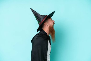 Cadılar Bayramı 'ndaki genç büyücü mavi arka planda izole edilmiş. Yan pozisyonda gülüyor.