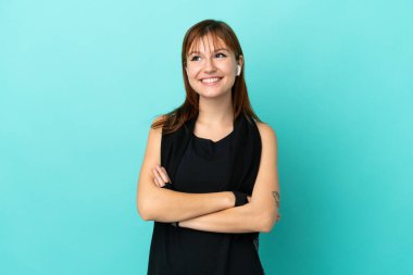 Kızıl saçlı sporcu kız mavi arka planda izole edilmiş gülümserken yukarı bakıyor