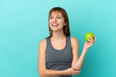 Redhead girl isolated on blue background with an apple and happy