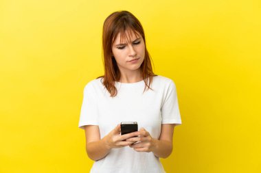Kızıl saçlı kız, sarı arka planda cep telefonu kullanarak izole edilmiş.