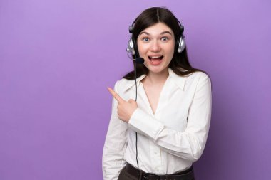 Mor arka planda izole edilmiş bir kulaklıkla çalışan pazarlamacı Rus kadın şaşırmış ve işaret ediyor.