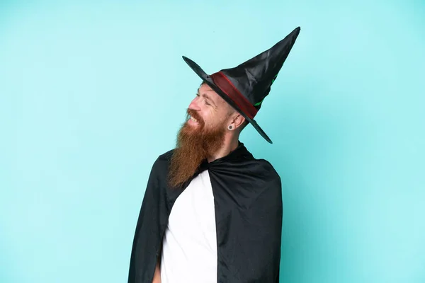 Young wizard in halloween isolated on blue background looking to the side and smiling