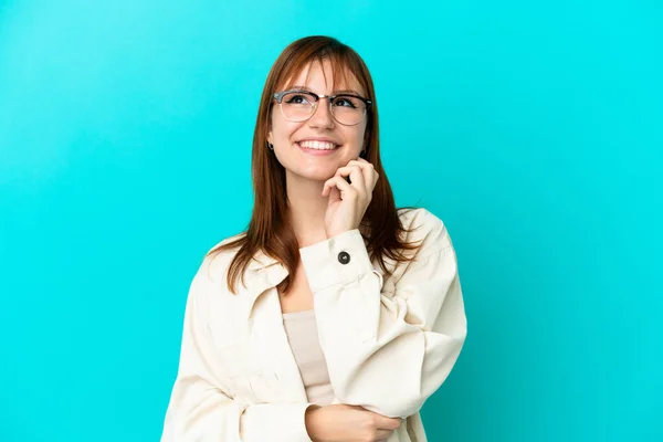 Roodharige Meisje Geïsoleerd Blauwe Achtergrond Met Bril Denken Terwijl Opkijken — Stockfoto