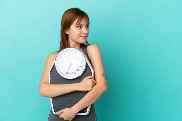 Roodharige Meisje Geïsoleerd Blauwe Achtergrond Met Weegmachine Zoek Kant — Stockfoto