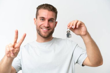 Young caucasian man holding home keys isolated on white background with thumbs up because something good has happened