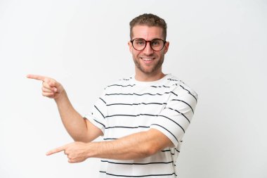 Beyaz arka planda izole edilmiş beyaz, yakışıklı beyaz bir adam parmağını yana uzatıp bir ürün sunuyor.