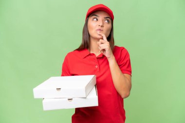 İş üniformalı beyaz bir kadın yeşil krom arka planda izole edilmiş pizza kutularını topluyor.