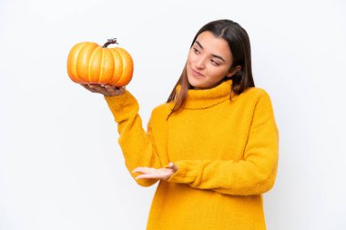 Beyaz arka planda izole edilmiş bir balkabağı tutan genç beyaz kadın davet etmek için ellerini yana uzatıyor.