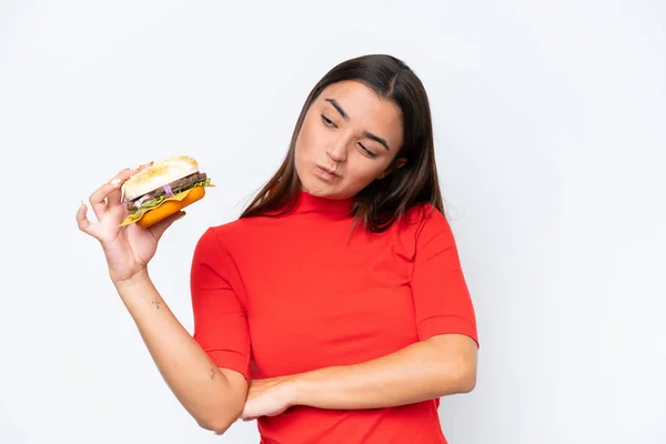 Młoda Kaukaska Kobieta Trzyma Hamburgera Białym Tle Smutnym Wyrazem Twarzy — Zdjęcie stockowe