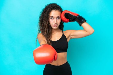 Genç Arap kadın mavi arka planda boks eldivenleriyle izole edilmiş.