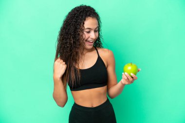 Yeşil arka planda izole edilmiş elmalı genç bir Arap kadın zaferi kutluyor.