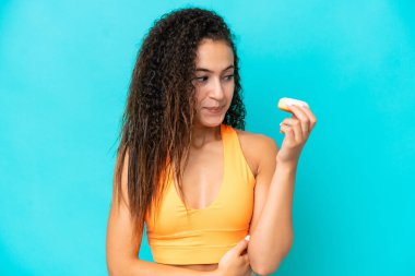 Genç bir Arap kadın mavi arka planda izole edilmiş, elinde donut var.