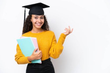 Arap üniversitesinden mezun bir kadın beyaz arka planda izole edilmiş kitapları tutuyor ve davet etmek için ellerini yana uzatıyor.