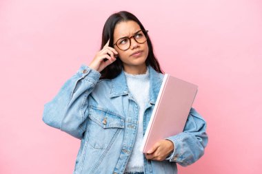 Pembe arka planda izole edilmiş genç Kolombiyalı kadın şüpheleri ve düşünceleri var.