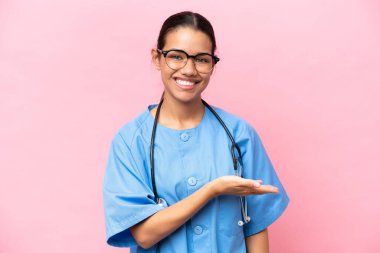 Pembe arka planda izole edilmiş genç Kolombiyalı hemşire gülümseyerek bir fikir sunuyor.