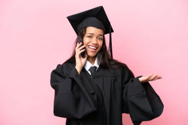 Pembe arka planda izole edilmiş genç Kolombiyalı bir kadın cep telefonuyla sohbet ediyor.