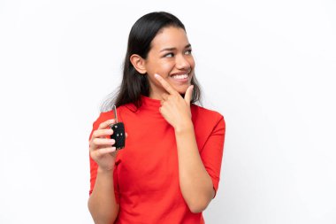 Beyaz arka planda araba anahtarı tutan genç Kolombiyalı kadın bir fikir üretiyor ve bakıyor.