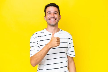 Izole sarı arka plan üzerinde genç yakışıklı adam jest kadar bir başparmak veren
